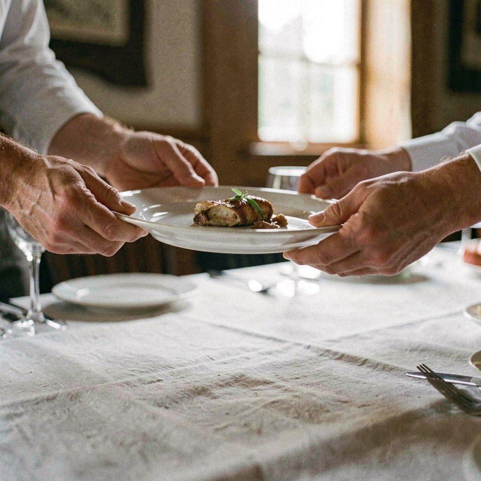 Mains relevant une assiette dressée au-dessus d’une nappe claire pendant le service d’un repas de réception.